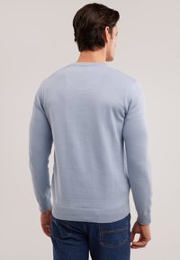 Suéter de punto azul claro con mangas largas y puños acanalados. Presenta un escote redondeado y un diseño sencillo sin patrones.