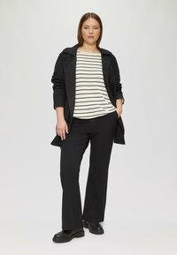 Manteau noir sur un haut rayé blanc et noir, associé à un pantalon noir et des chaussures noires robustes. Design simple et moderne.
