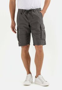 Graue Cargo-Shorts mit elastischem Bund und Kordelzug. Verfügt über zwei Seitentaschen und zwei Cargo-Taschen. Getragen mit weißen Turnschuhen.