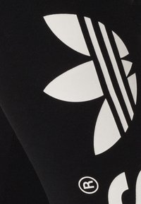 Černé legíny z elastické látky s velkým bílým květinovým logem a třemi pruhy podél boku.