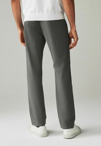 Pantaloni grigi con una vestibilità dritta, realizzati in un tessuto leggero, con una texture liscia e una cintura elastica, abbinati a sneakers bianche.