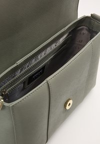 Borsa a tracolla verde con texture, dotata di chiusura a scatto dorata e diversi scomparti interni. Presenta un'etichetta con logo e una sfoderatura in tessuto liscio.