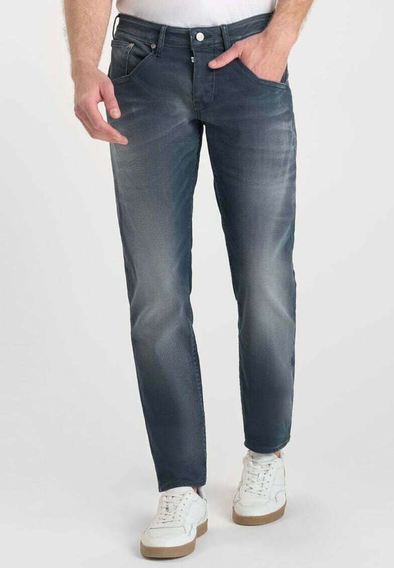 Vaqueros oscuros de hombre, diseño ajustado, textura desgastada, cinco bolsillos, cierre de botón de metal, combinados con zapatillas blancas.