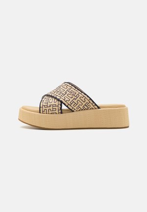 Beige Plattform-Sandalen mit Kreuzriemen, die ein geometrisches Muster mit schwarzen Umrandungen aufweisen. Texturierte Sohle für besseren Halt.