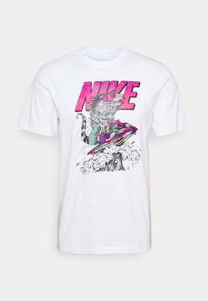 Valkoinen puuvillapaita, jossa on värikäs graafinen kuva iguanaan, joka soutaa vesiskootterilla. Paidan etuosassa on vaaleanpunaista "NIKE"-tekstiä ja "JUST DO IT." -slogan.