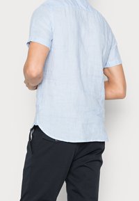 Lichtblauw linnen overhemd met korte mouwen, een licht gebogen zoom, zichtbare textuur en een button-down kraag, gecombineerd met een donkere broek.