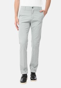 Pantaloni in cotone misto grigio chiaro con vestibilità slim, dotati di tasche laterali, chiusura con bottone e dettagli di cucitura minimi. Scarpe nere indossate.