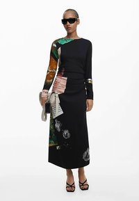 Rochie neagră cu mâneci lungi, cu imprimeuri mixte, motive florale și accente texturate. Include un detaliu argintiu și este asortată cu o geantă deschisă la culoare.