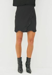 Black skirt with a scalloped hem, made from smooth fabric. Paired with glossy black ankle boots featuring metallic studs.