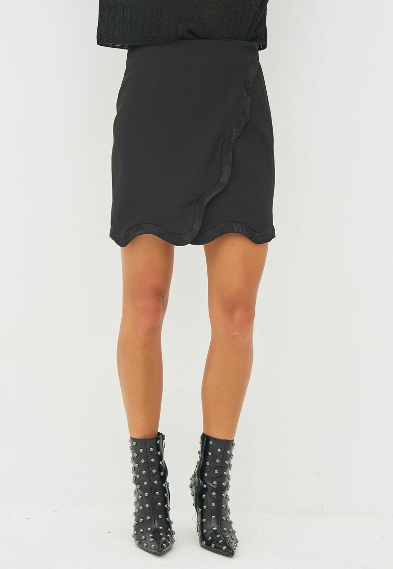 Black skirt with a scalloped hem, made from smooth fabric. Paired with glossy black ankle boots featuring metallic studs.