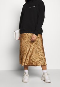 Czarna bluza z kapturem i troczkami oraz logo, w połączeniu z zwiewną brązową spódnicą w czarne kropki, dopełnioną białymi sneakersami.