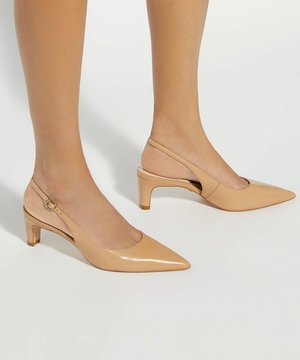Jambes portant des escarpins slingback couleur nude à bout pointu avec un talon bloc bas sur un fond clair.