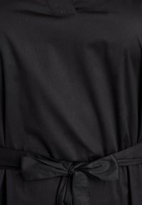 Nahaufnahme eines schwarzen Stoffkleides mit einem gebundenen Gürtel in der Taille, das die glatte Textur und subtile Nähdetails zeigt.