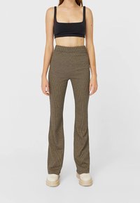 Top noir court et pantalon évasé à carreaux marron. Le pantalon a une taille haute, une texture lisse, et un motif subtil. Chaussures épaisses de couleur crème.