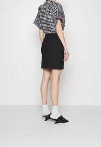 Gonna nera fino al ginocchio con tasca laterale, abbinata a una blusa a maniche corte a quadri. Indossata con calzini bianchi e mule nere con tacco.