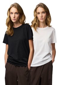 Fekete-fehér, kerek nyakú pólók puha pamut anyagból, enyhén bő szabásúak, csíkos barna nadrággal bemutatva.