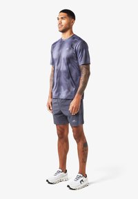 Completo sportivo maschile composto da una t-shirt in rete tie-dye blu navy, pantaloni corti grigi e sneaker bianche con dettagli neri e suola distintiva.