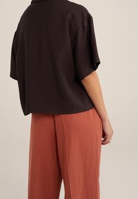 Top de manga corta, marrón oscuro, con un corte relajado y una tela texturizada. Combinado con unos pantalones holgados de color óxido.