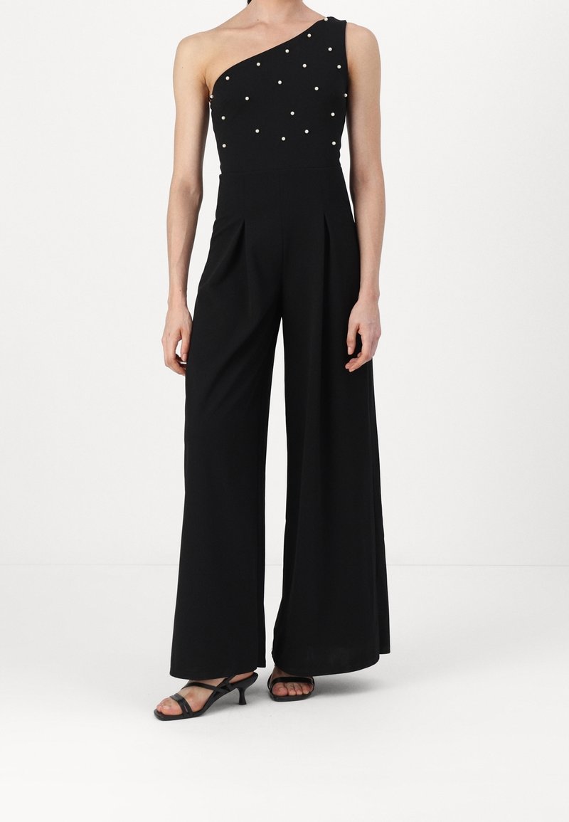 Zwarte jumpsuit met een asymmetrisch ontwerp met één schouder, versierd met witte parels, en brede pijpen. Gladde textuur.