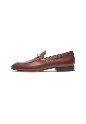 Mocassins en cuir marron avec des accents cousus, bout arrondi et petit talon empilé. Présente un détail de quincaillerie décoratif en or sur le dessus.