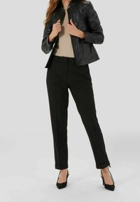 Veste en cuir noir au design ajusté, associée à un pantalon noir ajusté et des chaussures à talons hauts noires. Texture lisse et silhouette épurée.