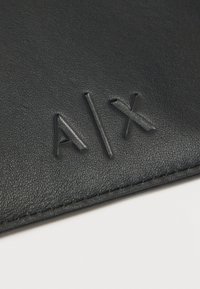 Μαύρη επιφάνεια από δέρμα με ανάγλυφο λογότυπο "A|X" και ορατό ράψιμο κατά μήκος της άκρης.