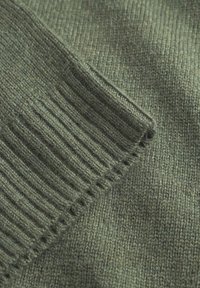 Grüner Strickstoff mit gerippten Bündchen und einer glatten Oberflächenstruktur, die eine Mischung aus feinen und groben Garnen in verschiedenen Farbtönen zeigt.