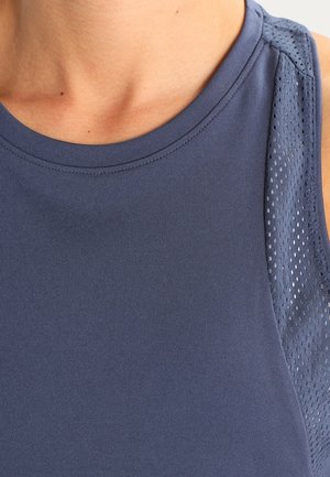 Lähikuva henkilöstä, joka käyttää hihutonta tummansinistä urheilupaitaa, jossa on verkkokangasta hartia-alueella.