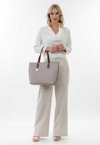 Sac fourre-tout avec motif géométrique gris, anses en cuir marron, forme rectangulaire et étiquette argentée. Modèle portant une tenue de couleur claire.