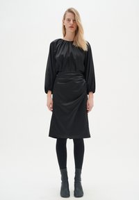 Mustat satiini mekko, jossa on kerätty kaula-aukko, pallokuosiset hihat ja laskostettu hame. Yhdistetty mustiin legginsseihin ja nilkkurit.
