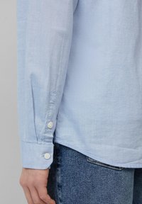 Lichtblauwe lange mouw overhemd met een gestructureerde stof, knopenmanchetten en een gebogen zoom, gecombineerd met denim jeans.