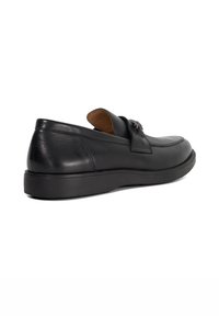 Black leather slip-on shoes with a flat rubber sole, featuring a smooth texture and a decorative buckle on the upper.