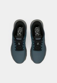 Ζευγάρι μπλε αθλητικά παπούτσια Skechers slip-on με μαύρα κορδόνια και γκρι σόλες, σε θέα από πάνω σε λευκό φόντο.