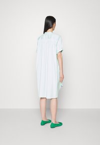 Robe vert menthe clair avec des manches courtes et roulées, et une coupe lâche et fluide. Associée à des ballerines vertes avec un accent en nœud.