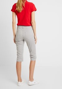 Harmaat caprihousut, joissa on kapea malli, valmistettu pehmeästä puuvillasta. Asua täydentää punainen lyhythihainen paita. Selkeä design, jossa näkyvät takataskut.