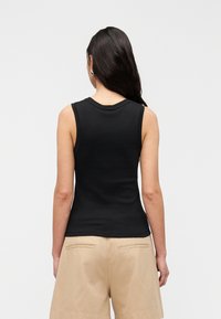 Μαύρο αμάνικο τοπ από βαμβάκι· διαθέτει στρογγυλή λαιμόκοψη και εφαρμοστή γραμμή, συνδυασμένο με μπεζ σορτς με τσέπες και άνετη εφαρμογή.