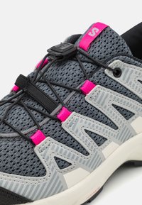 Šedá síťovaná turistická obuv s růžovými akcenty. Má elastické tkaničky, gumovou podrážku a pruhované designové prvky na boku pro lepší přilnavost.