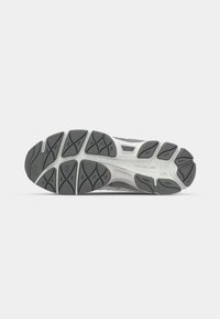 Semelle d'une chaussure de sport grise et blanche avec des motifs de bande de roulement texturés pour l'adhérence et l'amorti sur fond blanc uni.