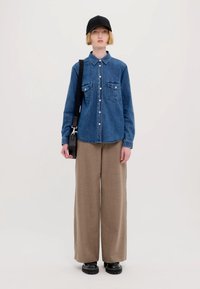 Δεμένο πουκάμισο τζην με δύο εσωτερικές τσέπες στο στήθος, συνδυασμένο με χαλαρούς μπεζ παντελόνες. Μαύρο καπέλο και τσάντα ώμου; χοντρά μαύρα παπούτσια.