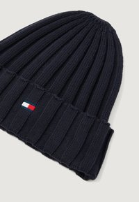 Mørkeblå ribbestrikket lue med brett, som har et lite rektangulært logo-patch i rød, hvit og blå.