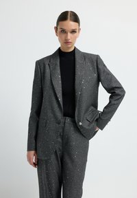 Grau kariertes Anzug mit silbernen Akzenten, bestehend aus einem strukturierten Blazer und passenden Hosen. Der Stoff hat ein strukturiertes Muster mit funkierenden Details.