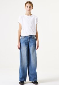 Camiseta blanca de manga corta combinada con jeans de pierna ancha de denim azul claro y sueltos. Zapatos negros con suela plana completan el atuendo.