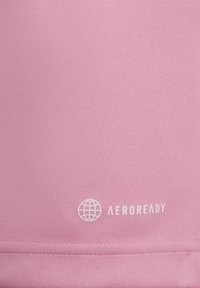 Roze stof met een gek textureerd oppervlak. Bevat een wit "AEROREADY" logo en een wereldbolontwerp nabij de zoom. Naaddetails zijn zichtbaar.