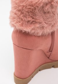 Botte compensée en daim rose avec un revers en fourrure duveteuse et une fermeture éclair latérale, dotée d'une semelle en caoutchouc et de détails cousus.