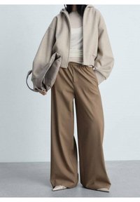 Sweat à capuche court beige avec une fermeture éclair, associé à un pantalon large marron et ample. Un sac à main gris doux complète la tenue.