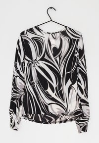 Blouse à manches longues avec motif floral noir et blanc, tissu léger, encolure ronde et détail noué à l'ourlet.