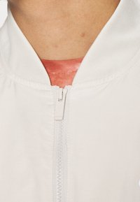 Gros plan d'une fermeture éclair blanche de veste fermée sur un sous-vêtement rouge avec une petite portion de cou visible au-dessus du col.