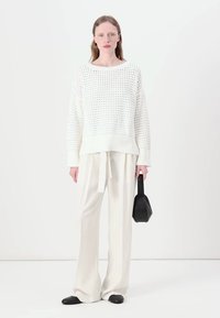 Maglione bianco lavorato a maglia con una vestibilità rilassata e orlo a coste, abbinato a pantaloni larghi color crema e una piccola borsa nera. Scarpe ballet flats nere.