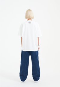 Vit oversized T-shirt med korta ärmar, baktryckt logotyp. Matchad med löst sittande mörkblå denimbyxor med tydliga bakfickor.