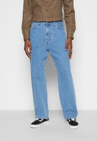 Vaaleansiniset denim-farkut rentoa istuvuutta, viisi-taskuista muotoilua ja suoria lahkeita, yhdistettynä mustiin ja valkoisiin lenkkareihin.